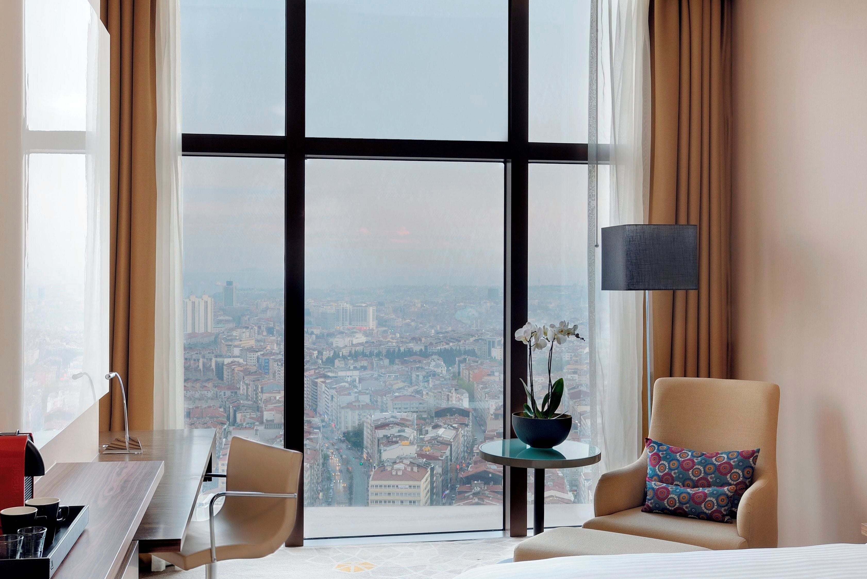 Una habitación de hotel con un ventanal grande, una cama, un escritorio y una silla.