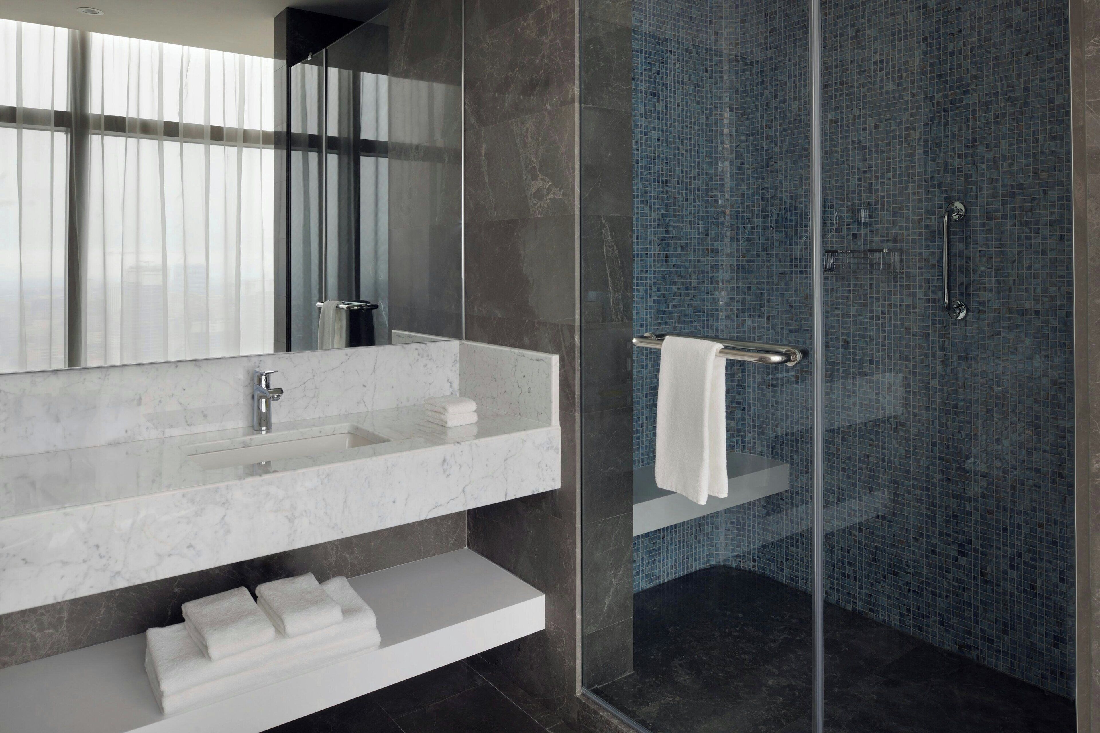 A modern bathroom with a glass shower enclosure, a marble sink, and a large mirror.
