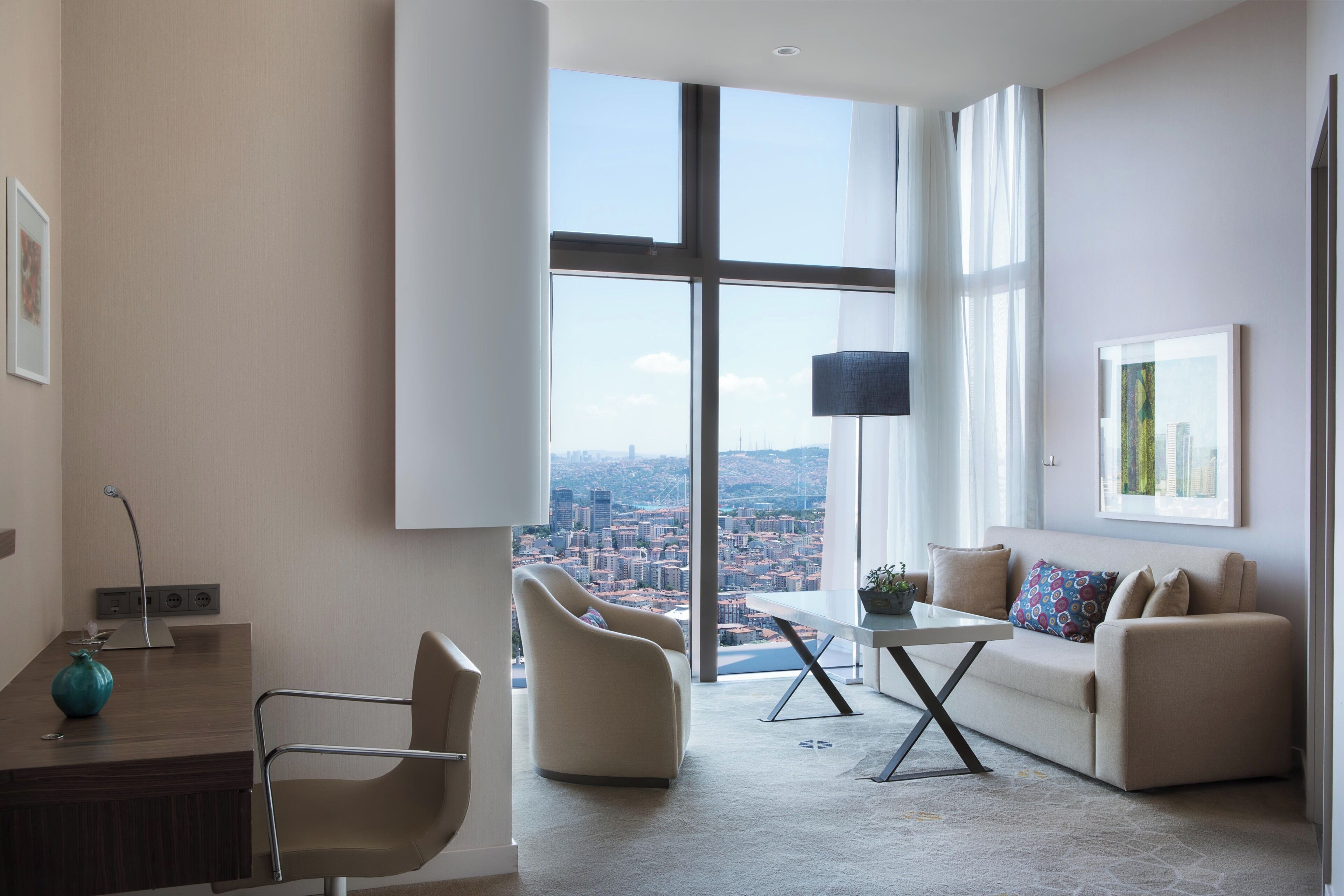 Ein modernes Wohnzimmer mit großem Fenster, einer Couch, einem Couchtisch und einem Schreibtisch mit Lampe.