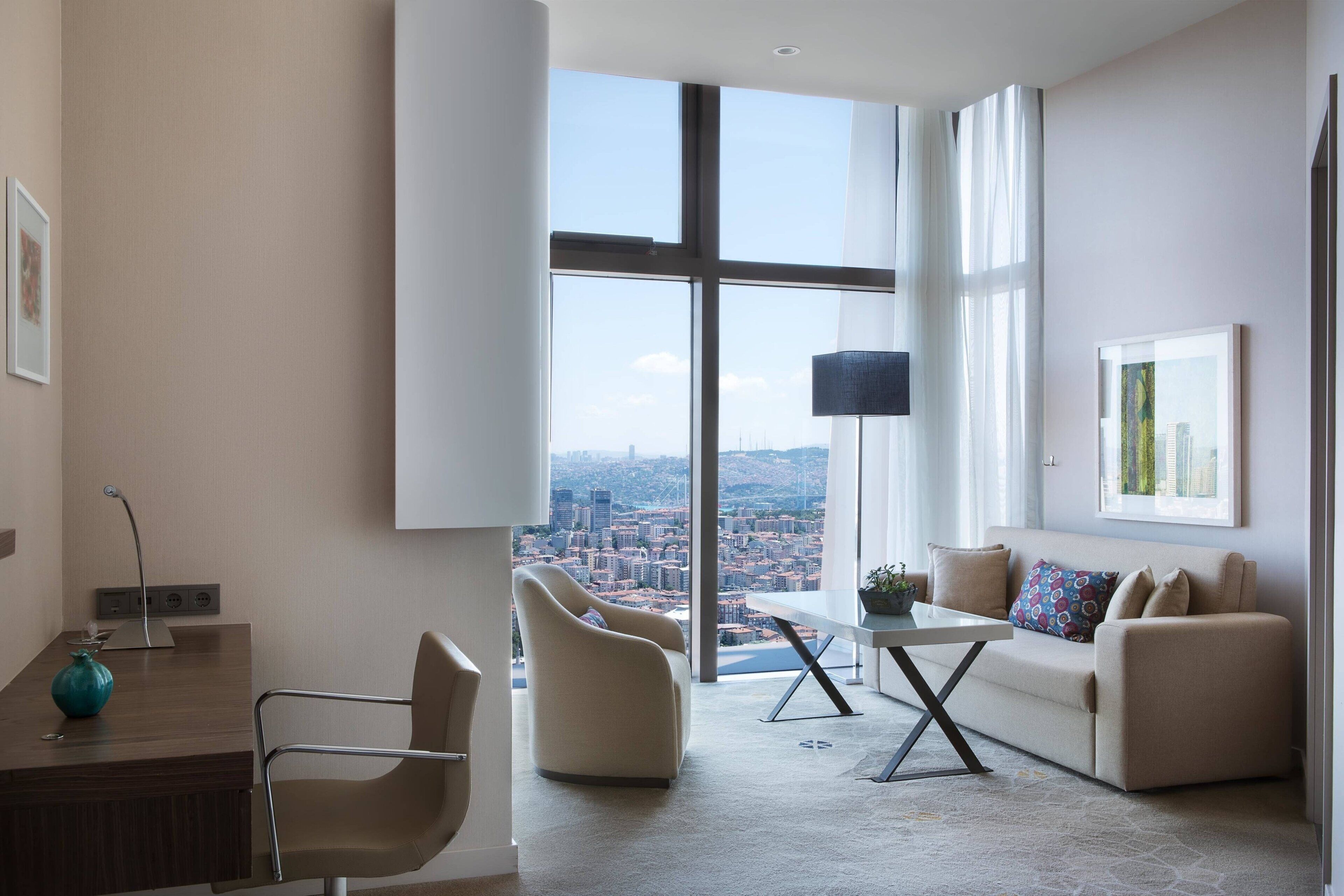 Una sala de estar moderna con un ventanal grande, un sofá, una mesa de centro y un escritorio con una lámpara.