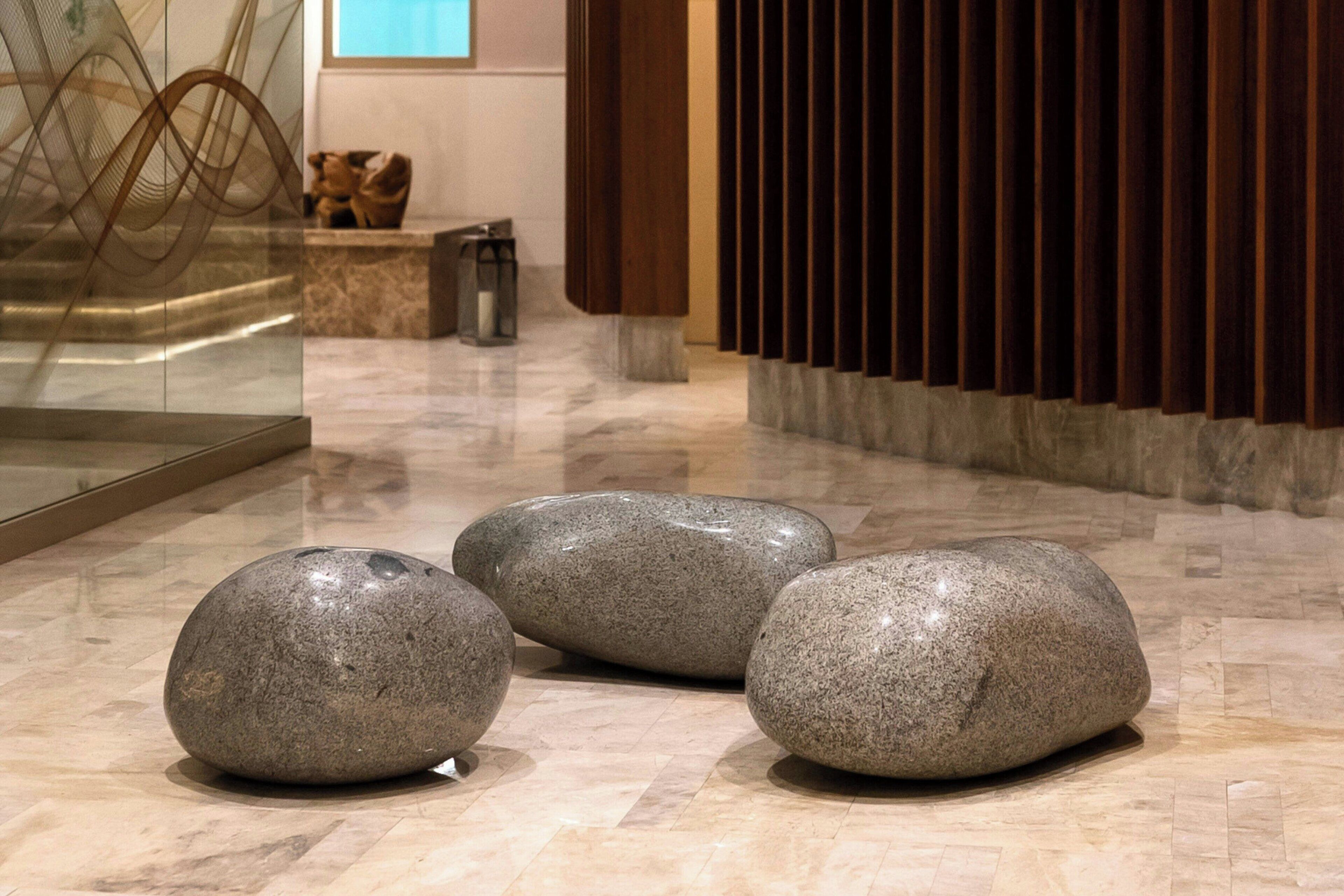 Trois grandes pierres polies sont disposées sur un sol brillant dans un hall d’entrée au design moderne, comprenant une cloison en verre et un panneau en bois.