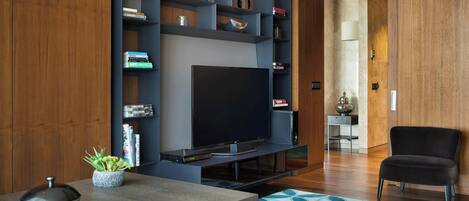 A modern living room with a flat-screen TV, a bookshelf, a coffee table, and a black chair.