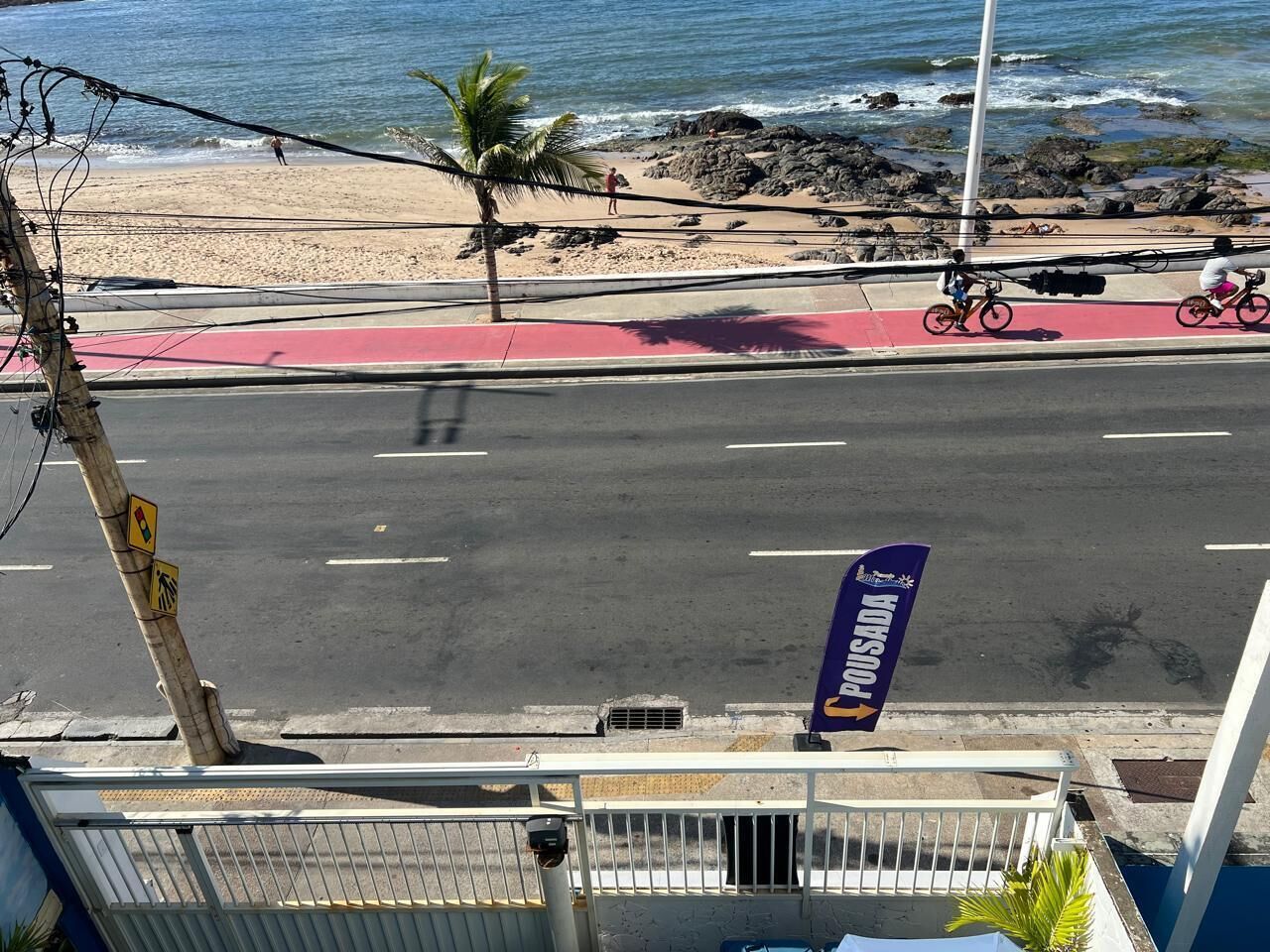 A beachside road with a red bike lane, a blue sign with 'PUSADA' text, and a view of the ocean and beach.