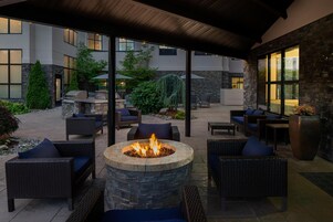 Un patio al aire libre con mobiliario de mimbre, un hogar de piedra y vistas a un edificio con amplias ventanas.
