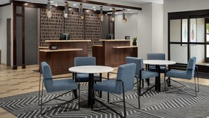 Un hall d’hôtel moderne avec un comptoir d’accueil, des fauteuils bleus, une table en marbre et un tapis à motifs.