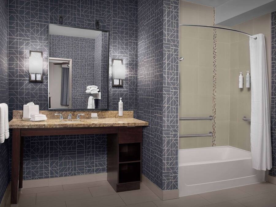 Un baño moderno con ducha de arco, azulejos oscuros con diseño, un tocador con espejo y un perchero para toallas.