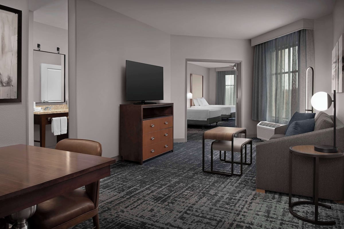 Ein Hotelzimmer mit einem Holztisch, einem Fernseher, einer Couch, einem kleinen Tisch und einem Bett.