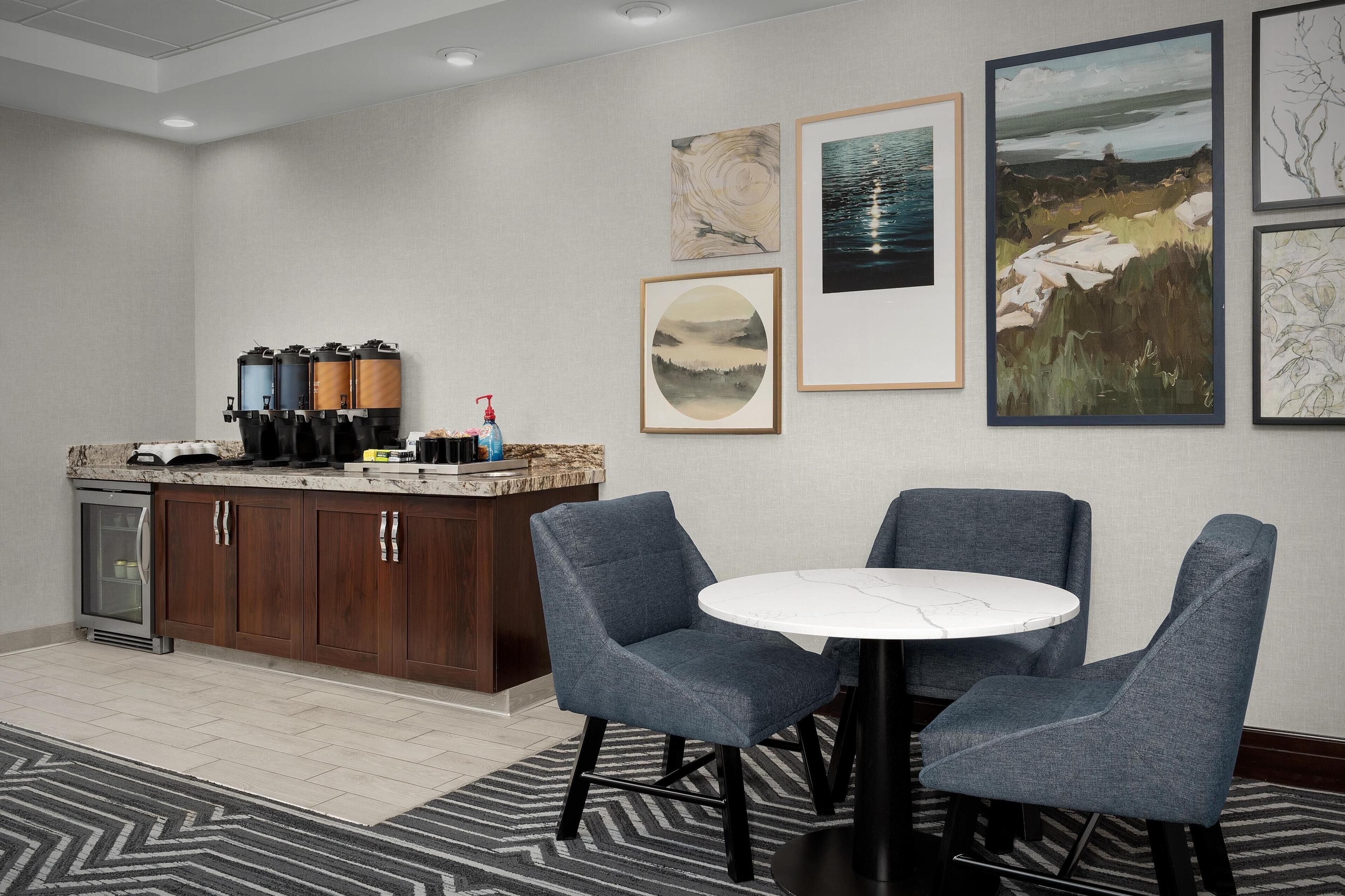 Una habitación de hotel con kitchenette, una mesa redonda con cuatro sillas y obras de arte en las paredes.