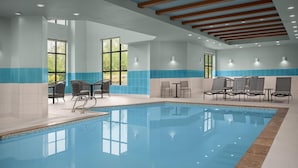 Une piscine intérieure à l’eau d’un bleu limpide, entourée de chaises longues et de tables, et dotée de grandes fenêtres qui laissent entrer la lumière naturelle.