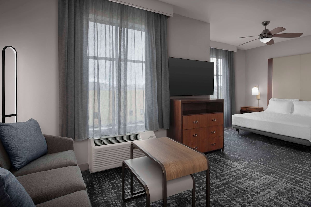 Ein Hotelzimmer mit Bett, Fernseher, Schreibtisch, Stuhl, Heizung und Deckenventilator.