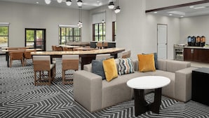Un hall d’hôtel moderne doté d’un grand espace salon, d’un coin cuisine et de grandes fenêtres laissant entrer la lumière naturelle.