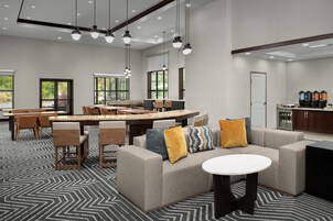 Un moderno vestíbulo de hotel con un amplio espacio para sentarse, una zona de cocina y grandes ventanales que aportan luz natural.