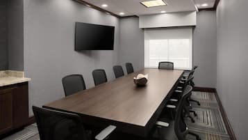 A conference room with a long table, chairs, a flat-screen TV, and a window.