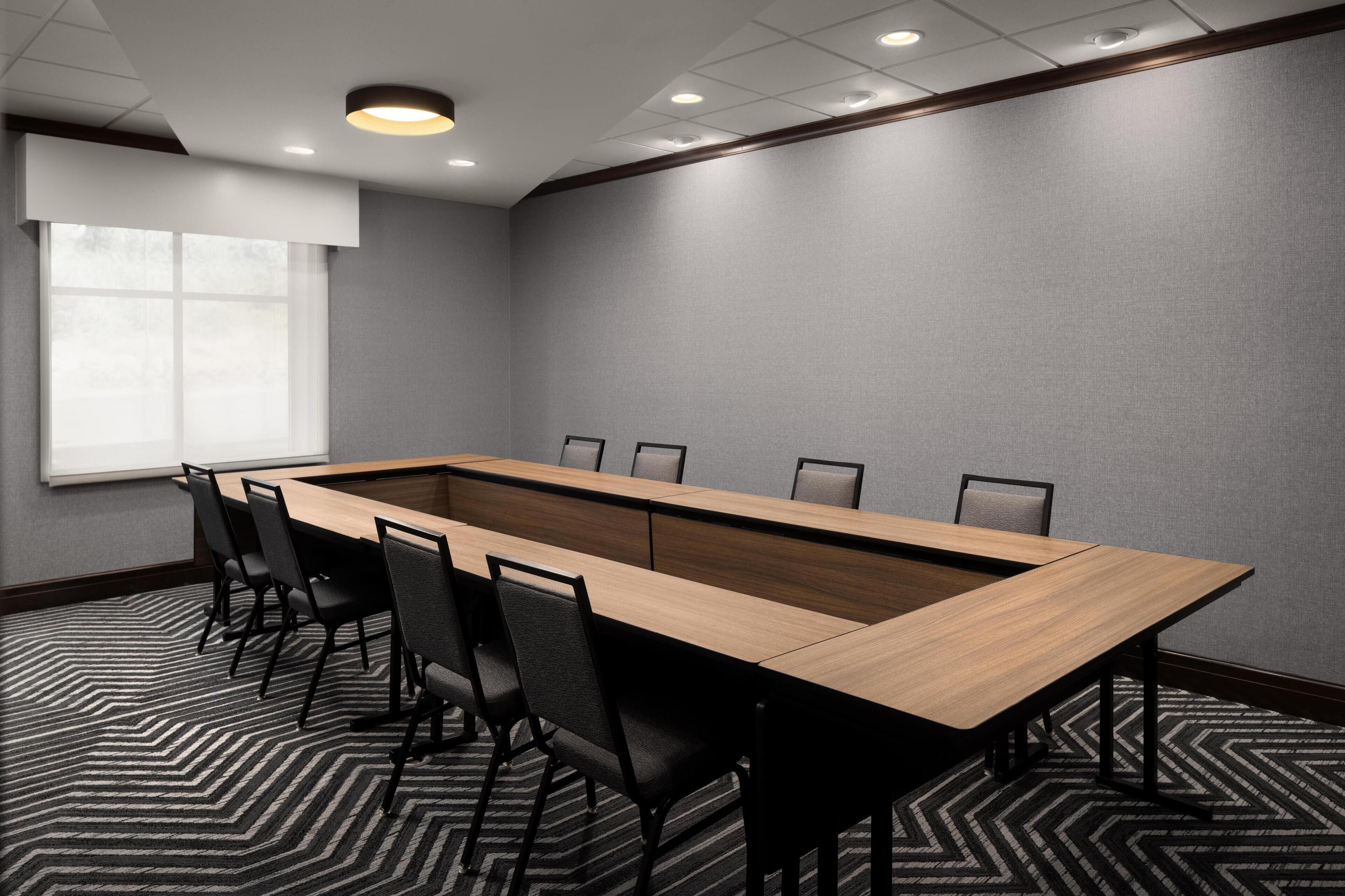 A conference room with a long table, chairs, a projector screen, and a window.