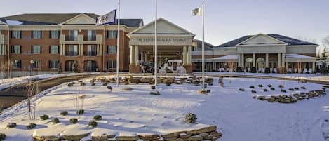 A hotel with a brick facade, a covered entrance, and a snow-covered landscape with stone planters and a flagpole.