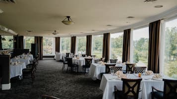 A dining area with tables set for service, large windows offering a view of the outdoors, and a carpeted floor.