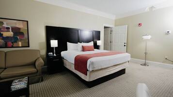 A hotel room with a bed, a nightstand, a chair, a painting, and a door.