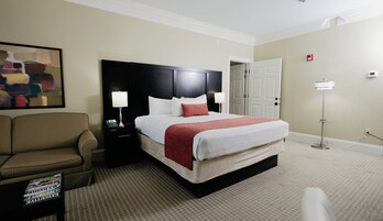 Una habitación de hotel con cama, mesita de noche, silla, un cuadro y una puerta.