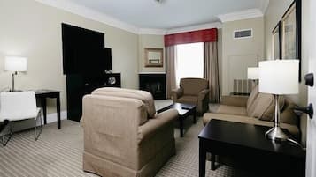 A hotel room with a sofa, armchair, and a small table. There is a television on the wall and a fireplace.