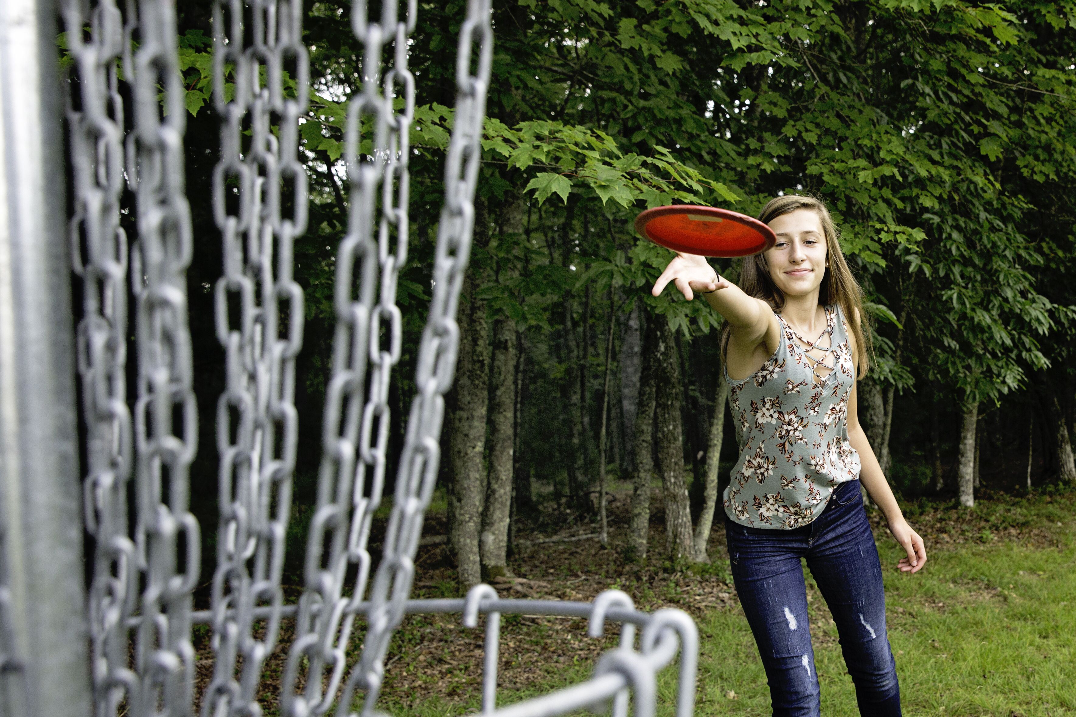 A person holding a frisbee near a chain-link fence in a wooded area.
