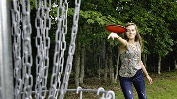 A person holding a frisbee near a chain-link fence in a wooded area.