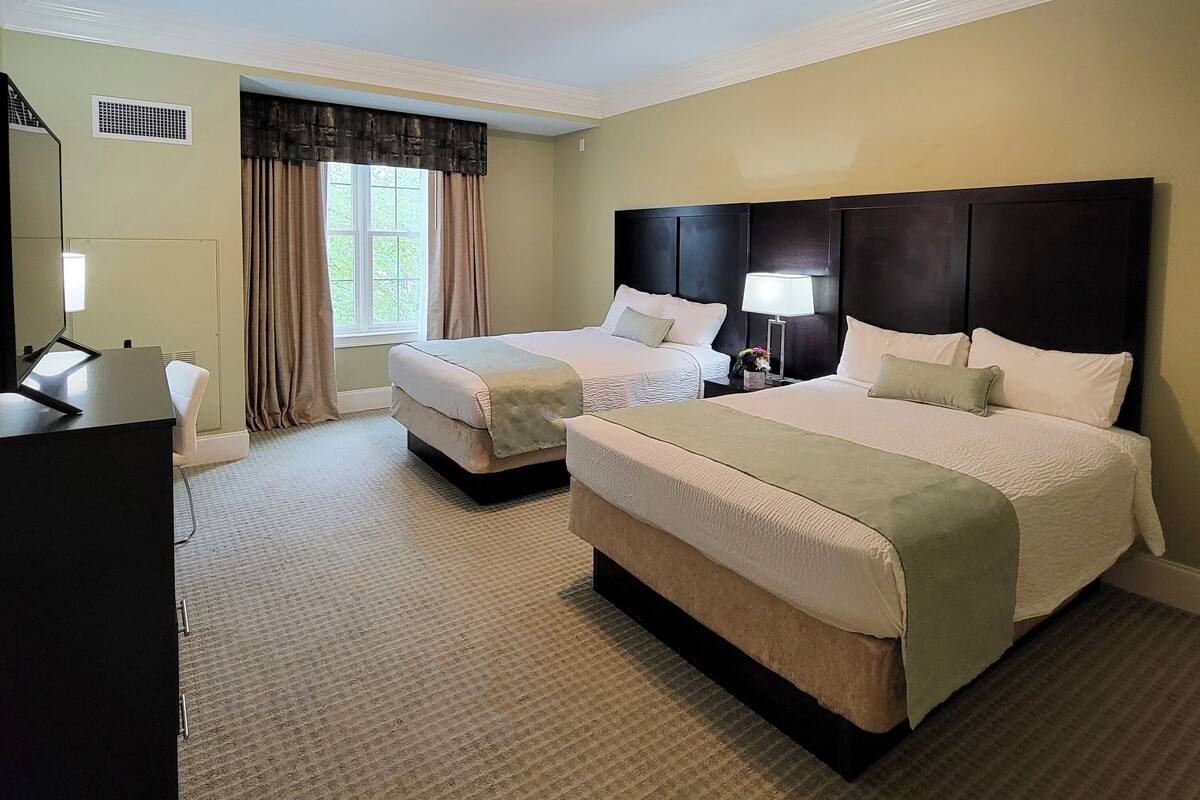 A hotel room with two beds, a desk, and a window with curtains.