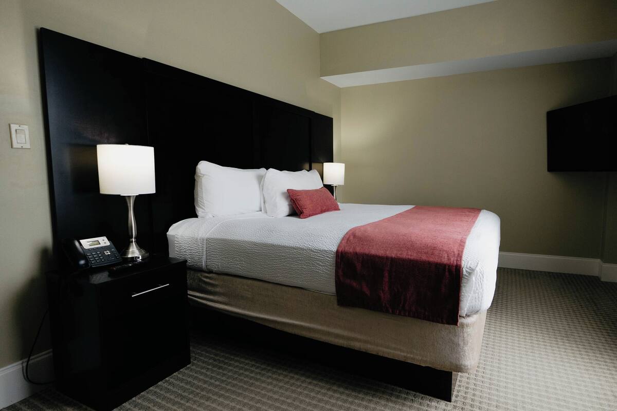A hotel room with a bed, two bedside lamps, a telephone, a flat-screen TV, and a carpeted floor.