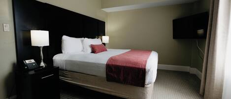 A hotel room with a bed, two bedside lamps, a telephone, a flat-screen TV, and a carpeted floor.