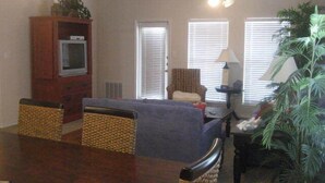 A living room with a blue sofa, a wooden cabinet, a ceiling fan, and a large plant. - The Rental Management Company (Corpus Christi)