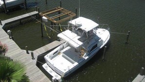A boat docked at a marina with a wooden deck, a covered seating area, and a small cabin. - The Rental Management Company (Corpus Christi)