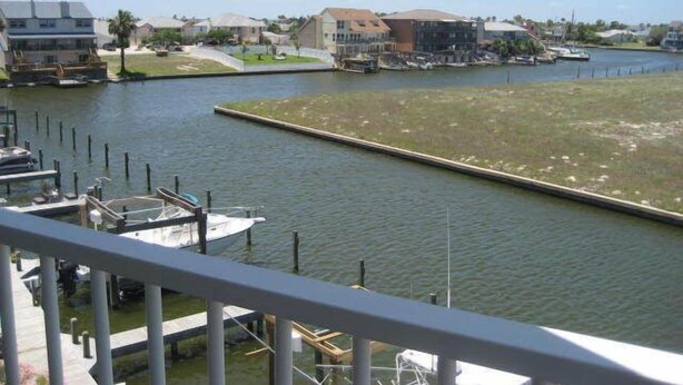 A marina with boats docked, a grassy area, and buildings in the background. - The Rental Management Company (Corpus Christi)