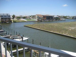 A marina with boats docked, a grassy area, and buildings in the background. - The Rental Management Company (Corpus Christi)