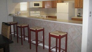 A kitchen with a central island, wooden cabinets, a microwave, and a refrigerator. - The Rental Management Company (Corpus Christi)