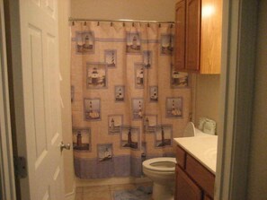 A bathroom with a patterned shower curtain, a toilet, and wooden cabinets. - The Rental Management Company (Corpus Christi)