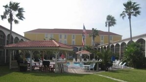 A hotel courtyard with a swimming pool, outdoor seating, and palm trees. - The Rental Management Company (Corpus Christi)