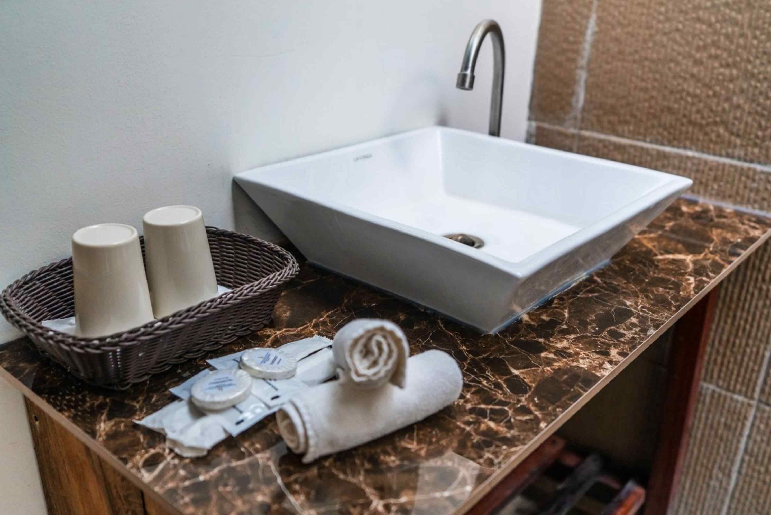 A bathroom with a white sink, a marble countertop, a wicker basket with toiletries, and a towel.