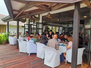 An outdoor dining area with tables covered in white tablecloths, wooden flooring, and a thatched roof structure. - Romantic Beach Villas Siargao Island (General Luna)