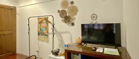 A room with wooden flooring, a television on a wooden stand, a small refrigerator, and a wall-mounted artwork.