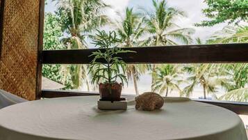 A round table with a potted plant and a small animal on it, viewed through a window with a view of palm trees.