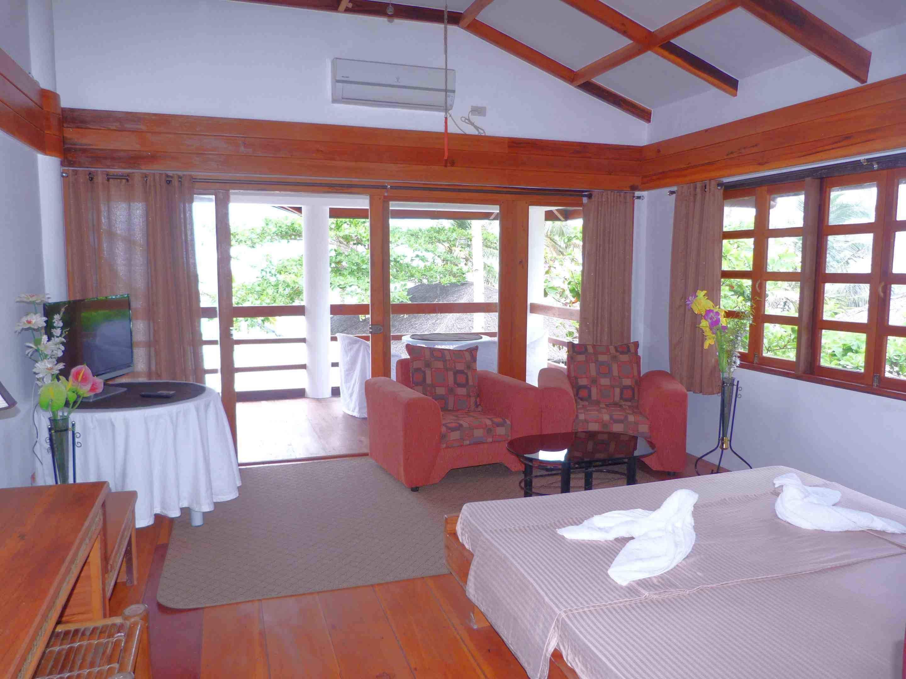 A room with a bed, a sofa, a small table, a television, and a window with curtains.