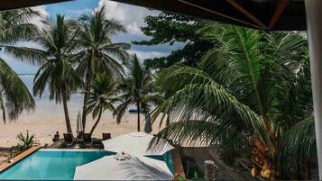 A pool area with lounge chairs and umbrellas, overlooking a beach with palm trees and a calm sea.