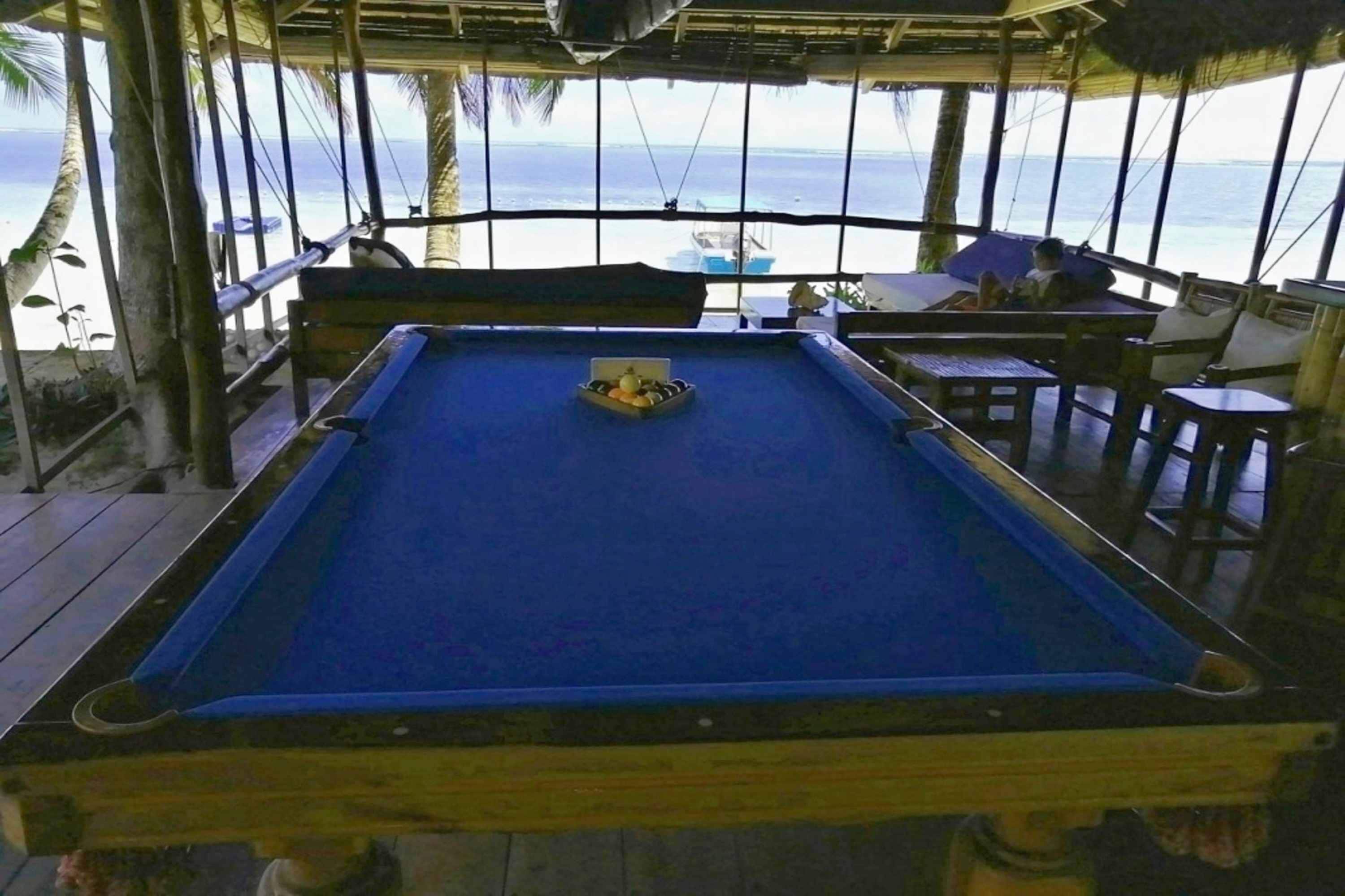 A pool table with a blue felt surface, surrounded by wooden furniture and a view of the ocean.