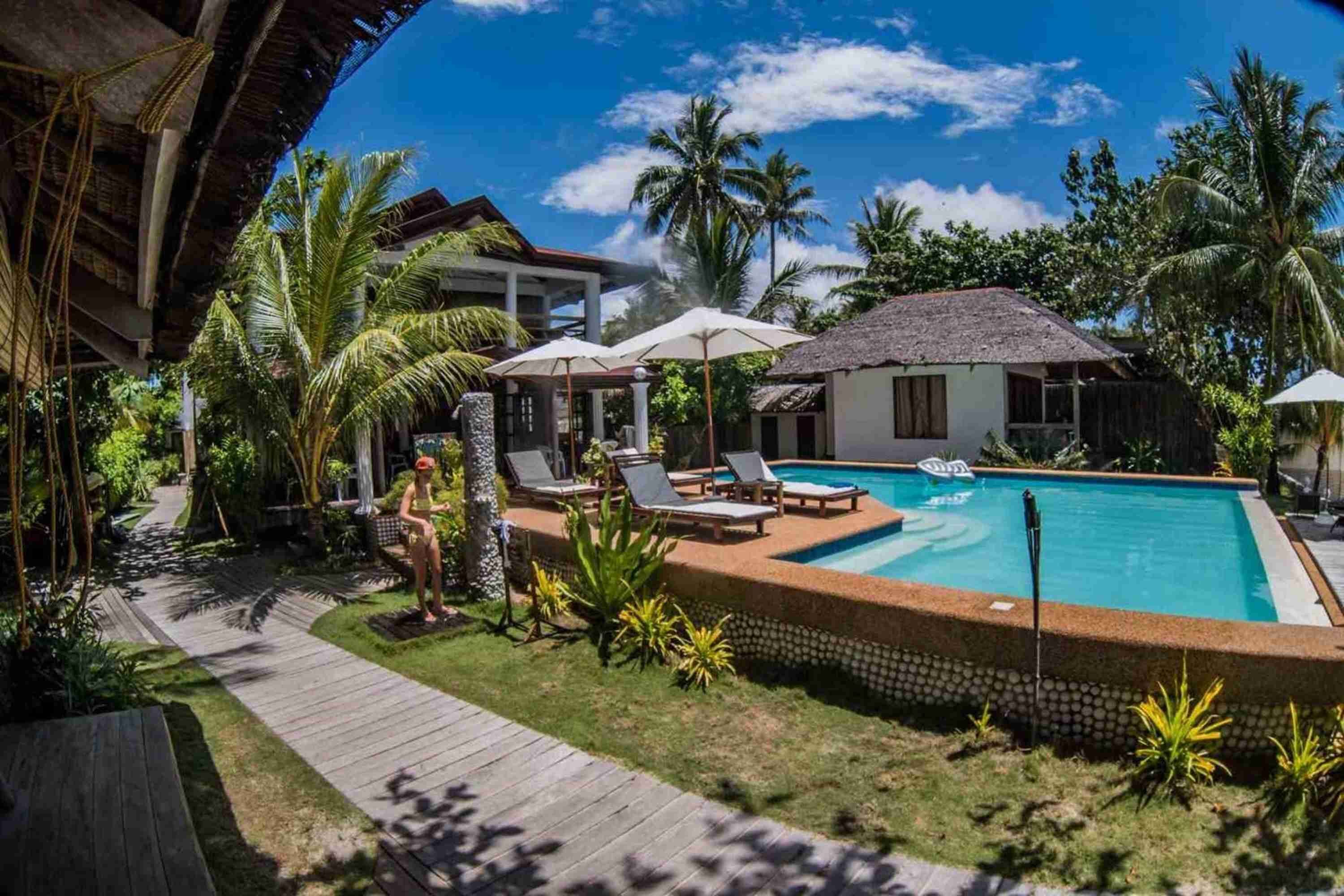 A pool area with lounge chairs and umbrellas, surrounded by palm trees and a wooden deck.