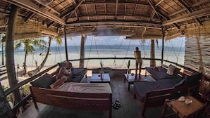 Un salón al aire libre con mobiliario de madera y vista a la playa.