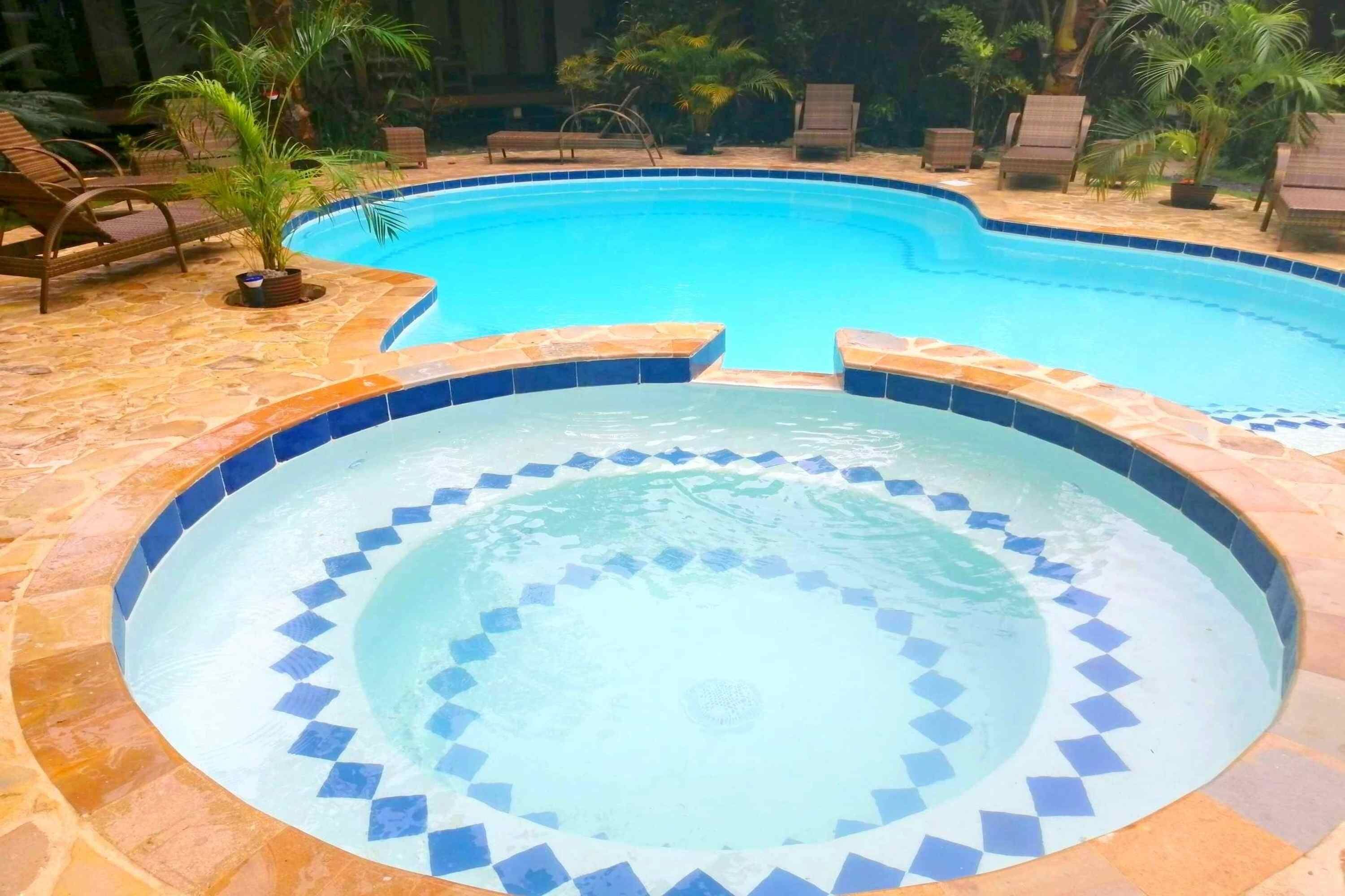 A circular hot tub with a blue mosaic border, surrounded by lounge chairs and palm trees.