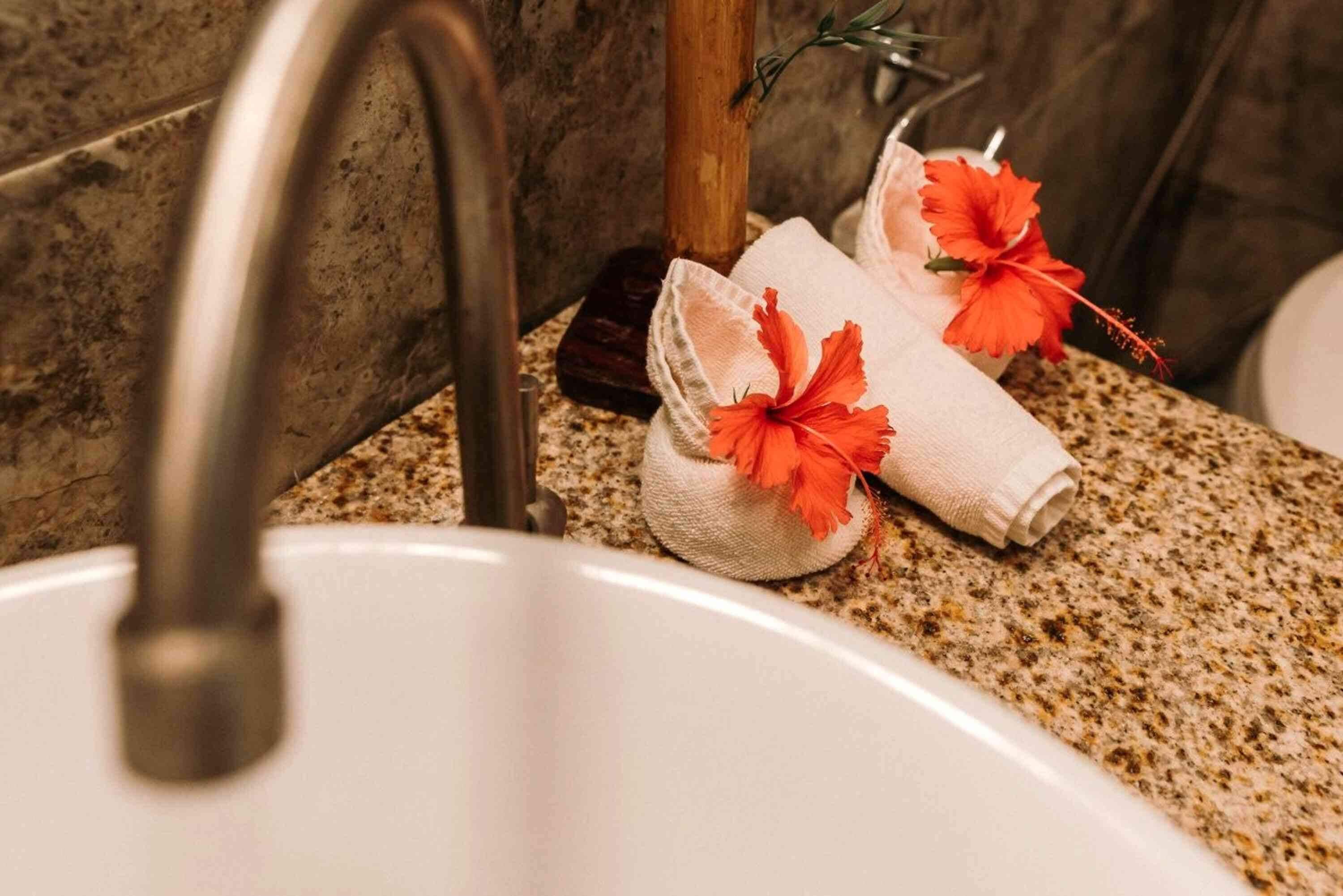 A bathroom sink with a granite countertop, a wooden towel holder, and two towels with hibiscus flowers.