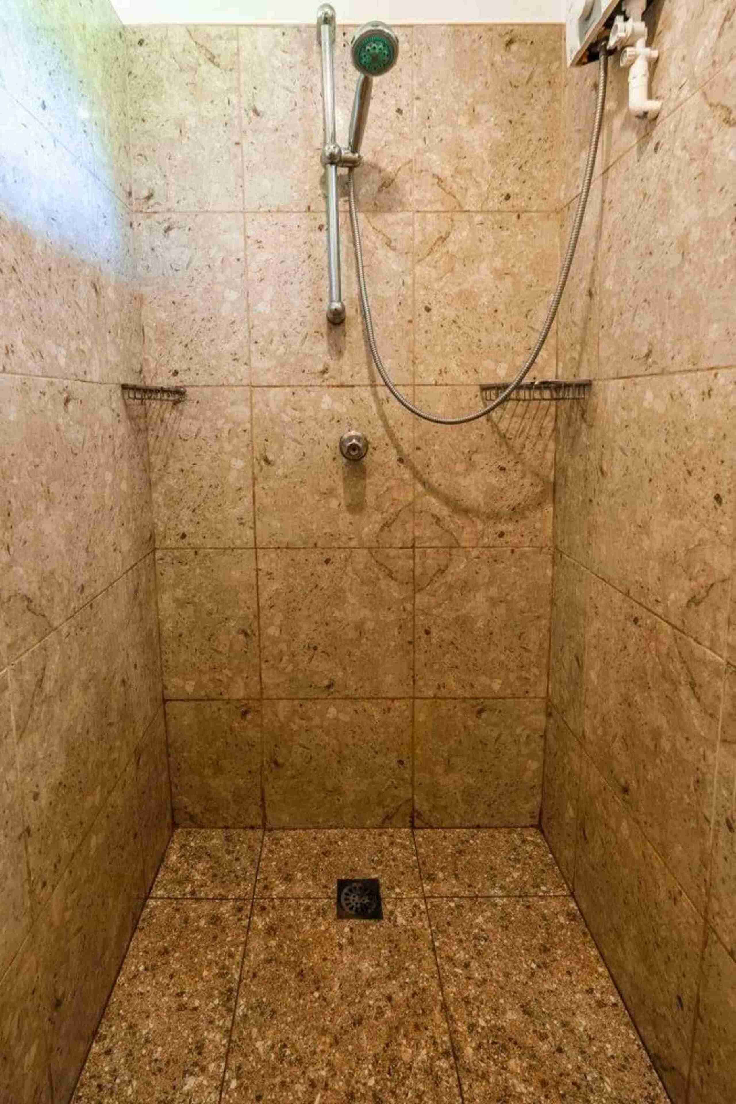 A small, tiled shower stall with a handheld showerhead and a drain in the center.
