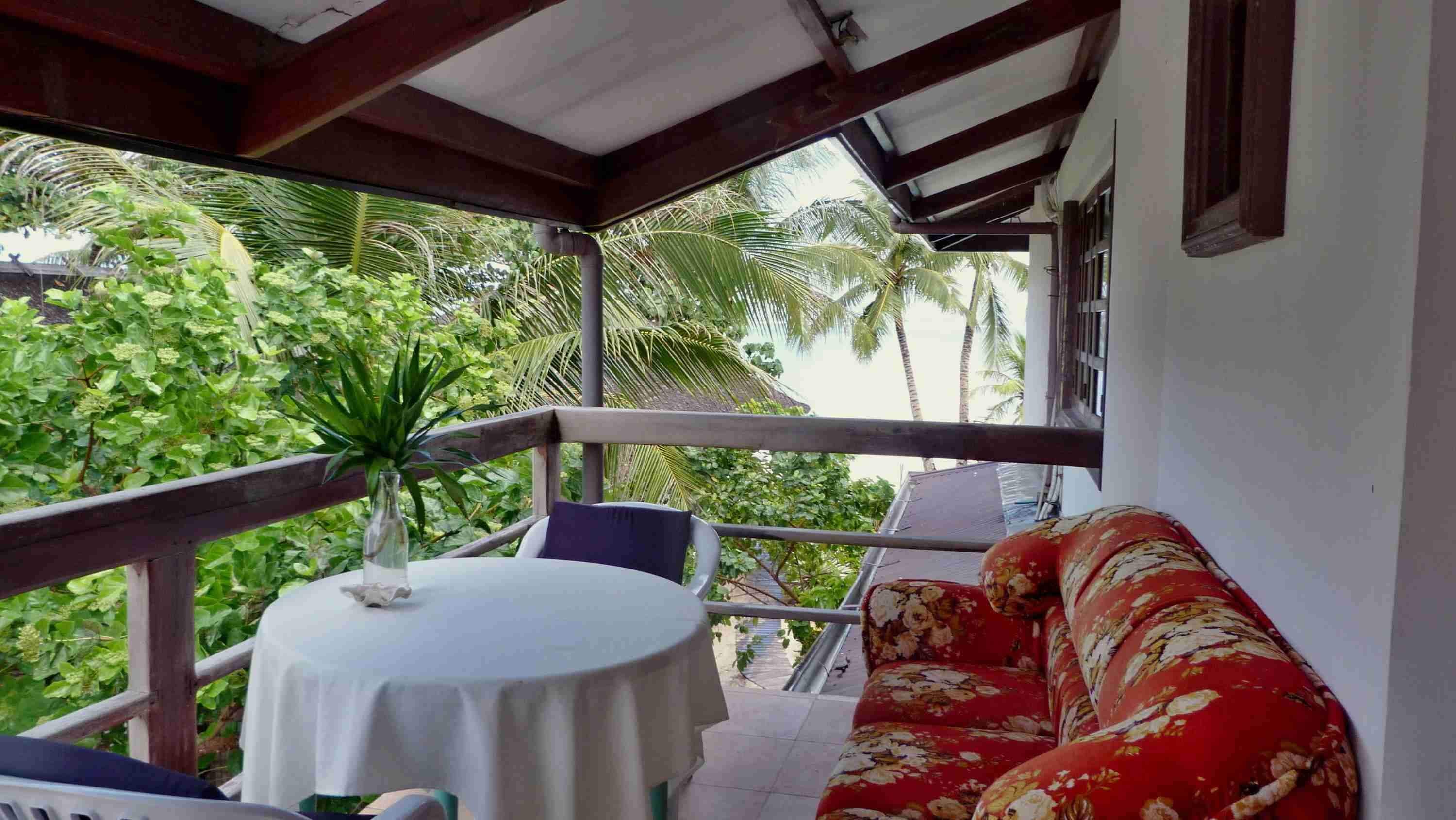 Un balcon agrémenté d’une table ronde et d’un canapé, entouré d’une végétation luxuriante et de palmiers.