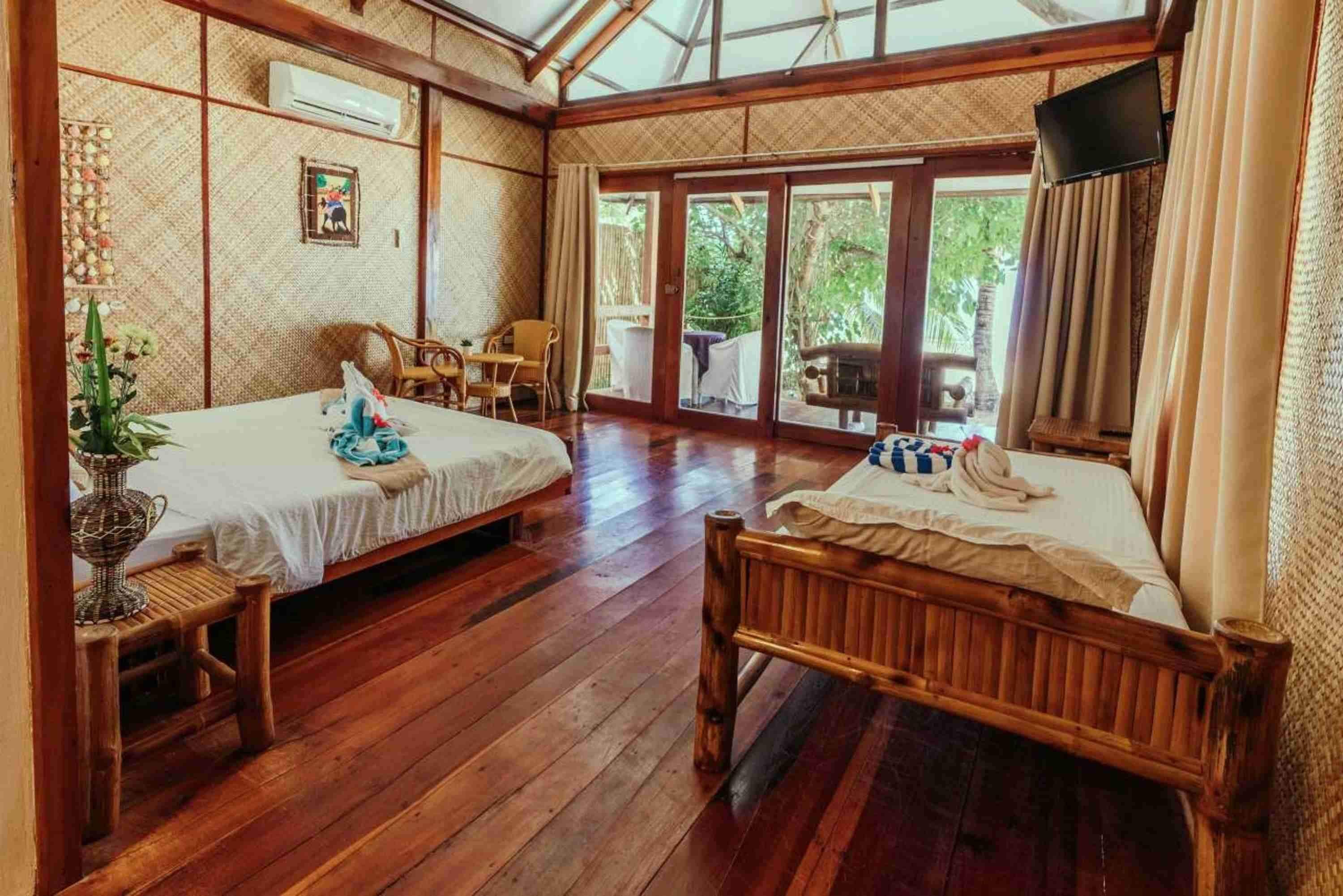 Habitación con dos camas de madera, un televisor y un amplio ventanal corredero que da a un espacio exterior.