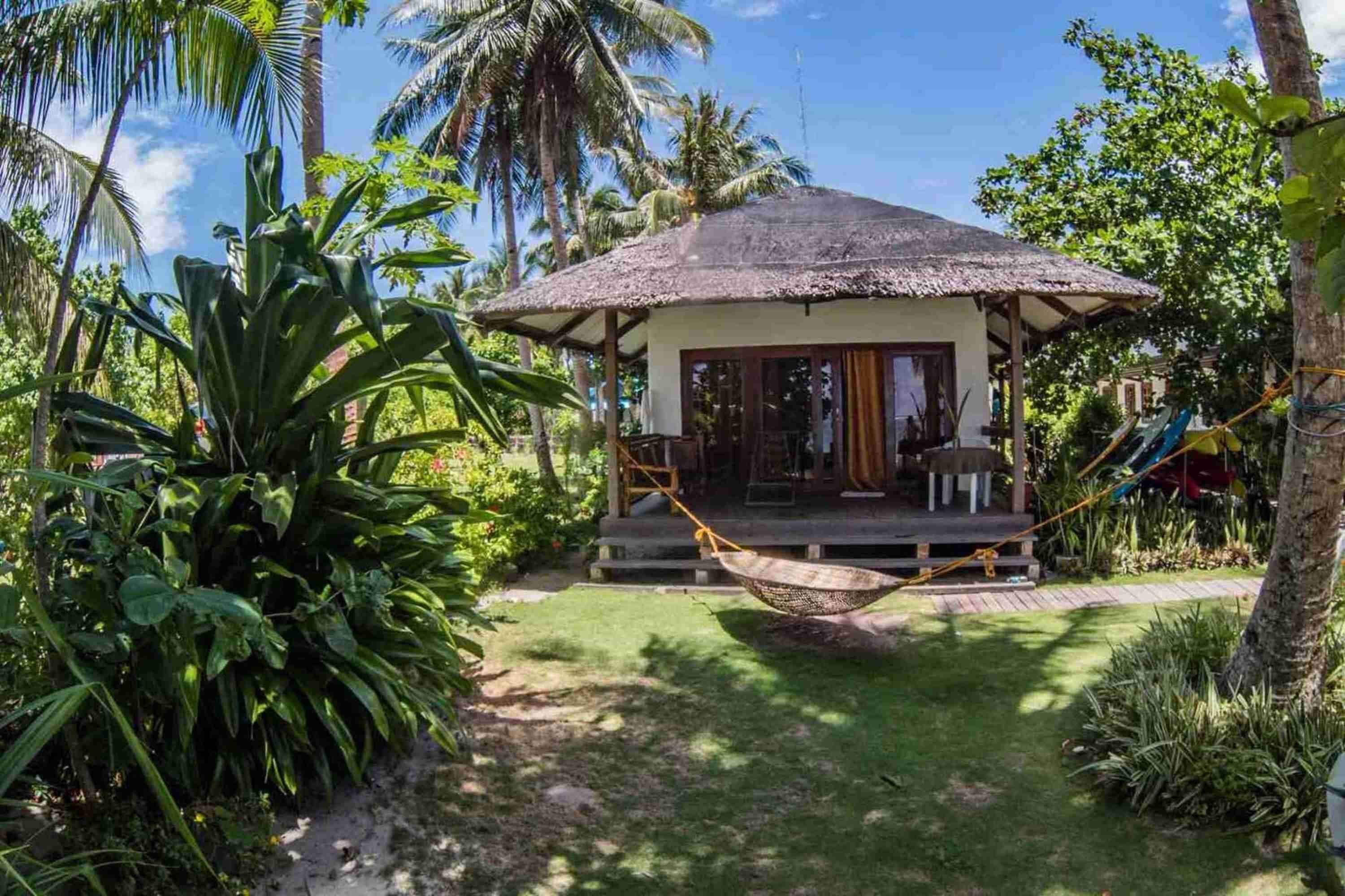 A thatched-roof hut with a porch, surrounded by lush tropical vegetation.